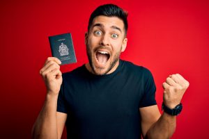 Young handsome tourist man holding canada canadian passport id over red background screaming proud and celebrating victory and success very excited, cheering emotion